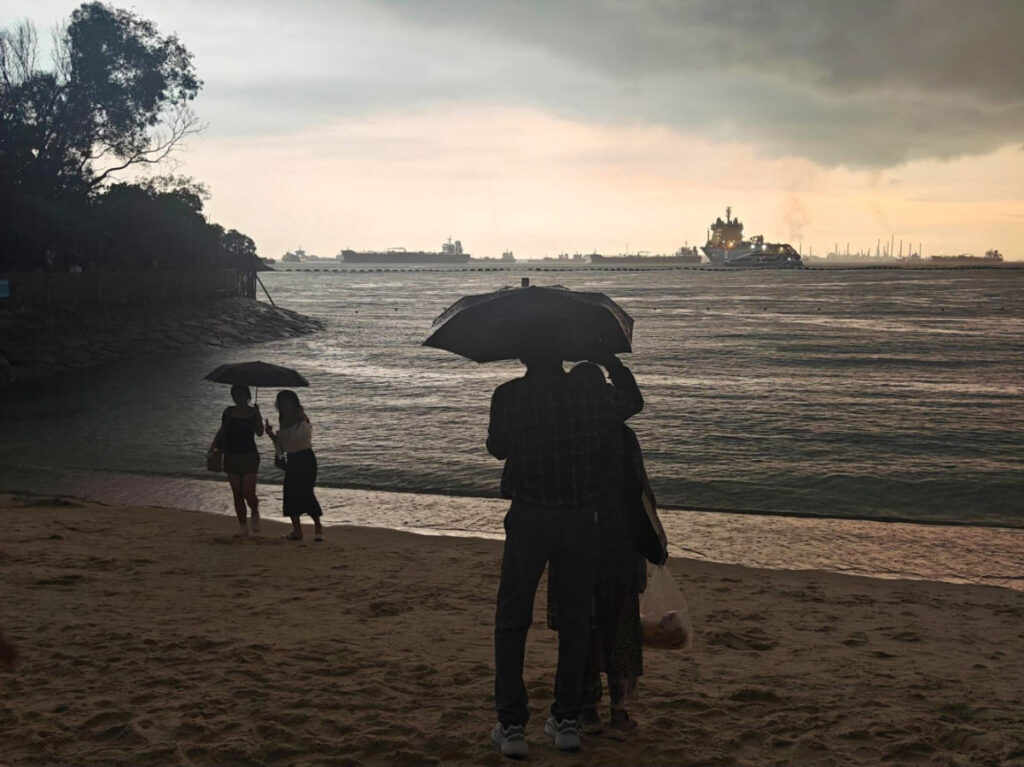 Beach goers holding umbrellas because of the rain at Siloso Beach
