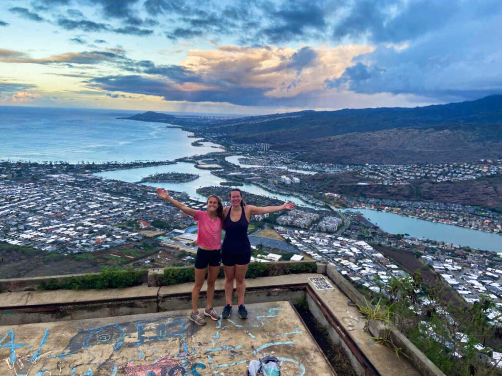 The author Rebecca Parsons with her friend posing for a photo with an overlooking view from the top of the Koko Crater Stairs