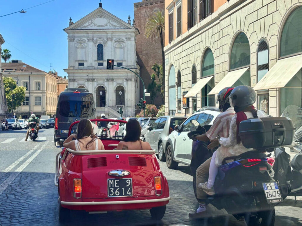 View of the tourists in a red slugbug driving in Rome