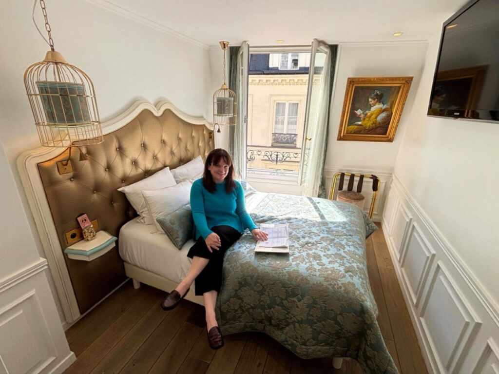 Travel Lemming writer Rachel perusing the welcome book on the cozy bed of Hôtel Académie Saint-Germain