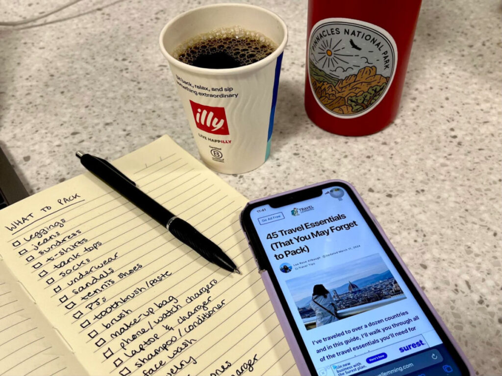 Written Travel packing lists, pen, and phone on a counter.