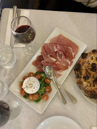 A rectangular plate with truffle burrata and prosciutto with flatbread on the table
