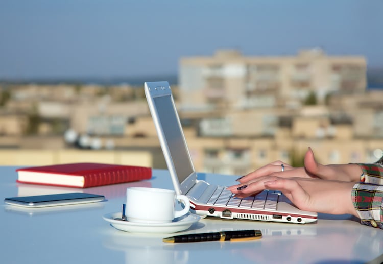 Close up and side view of female hands typing on laptop keyboard outdoors