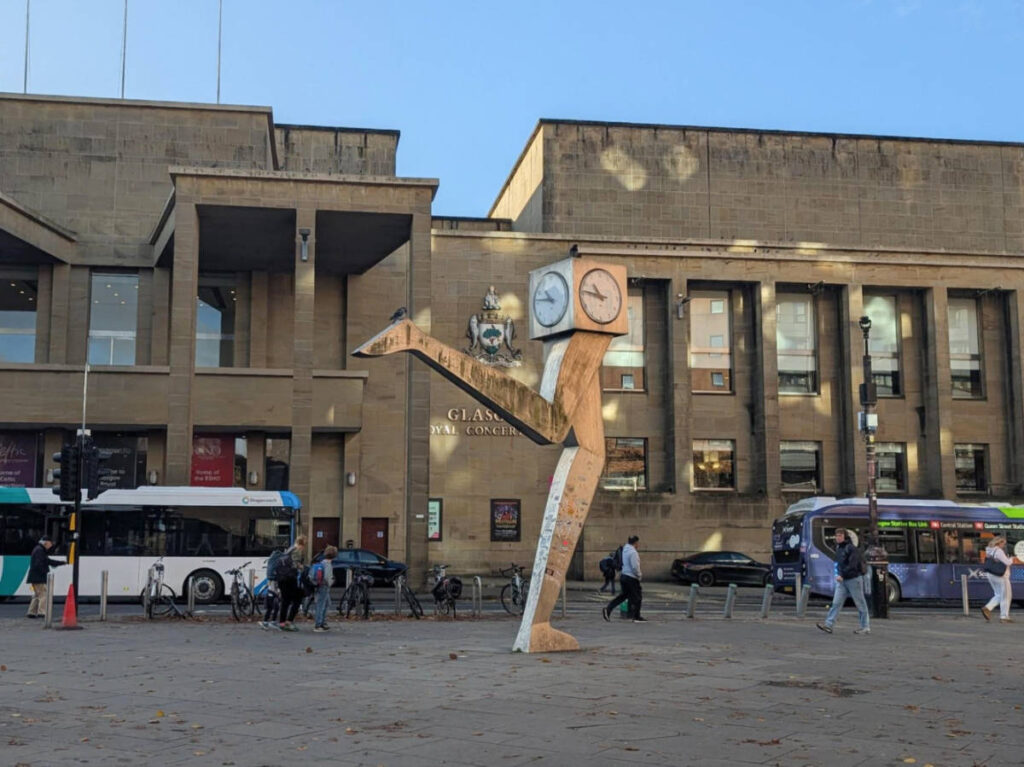 A unique sculpture with a clock on top in the middle of the street