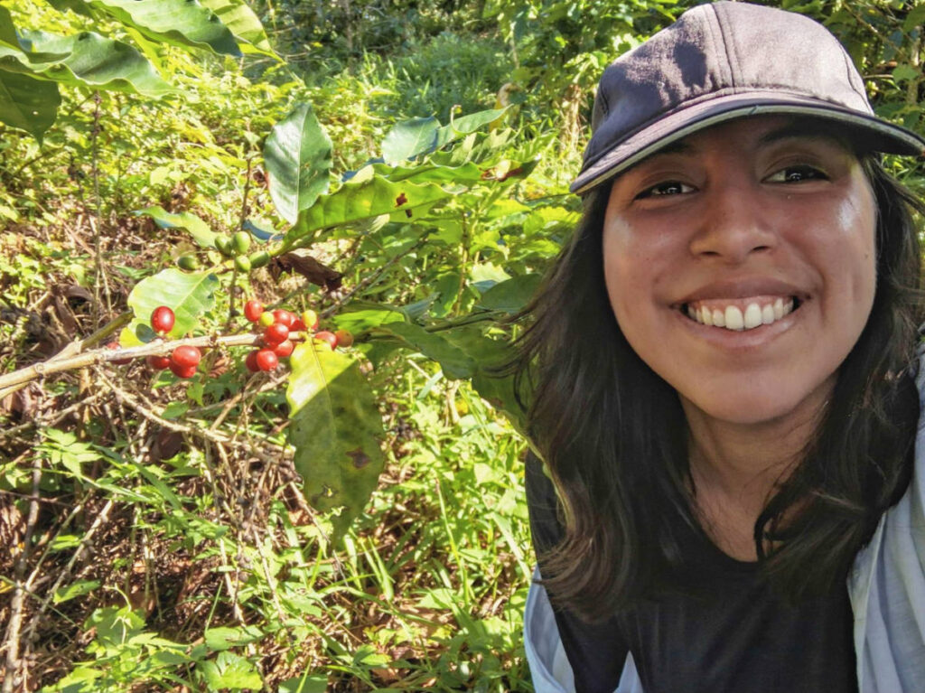 The author Vanessa Ramos, smiling for a photo in front of the coffee fruit at the farm