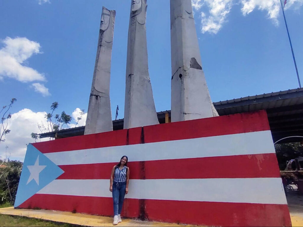 The author Vanessa Ramos, posing for a photo in front of the huge Puerto Rico flag at the Pork Highway