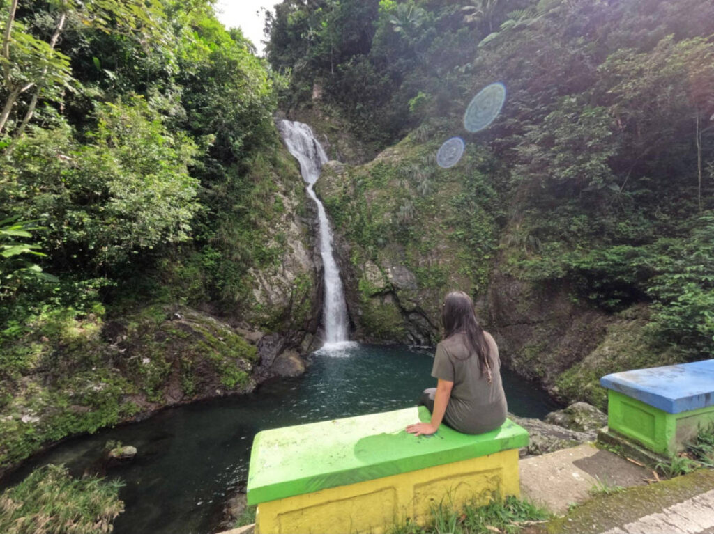 The author Vanessa Ramos, sitting on a bench while admiring the waterfalls in Doña Juana Waterfall