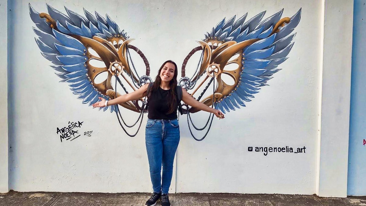 Travel Lemming Writer, Vanessa posing with a wing style mural in Paseo de Las Alas