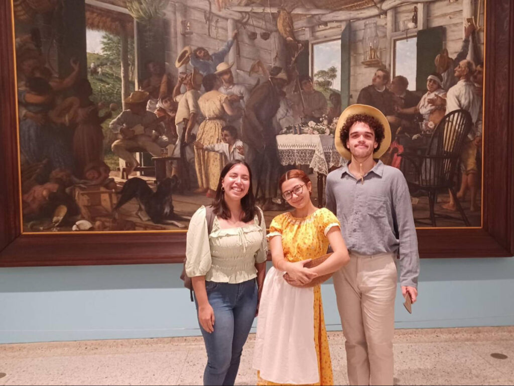 The author Vanessa Ramos, smiling for a photo in front of El Velorio by Francisco Oller