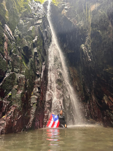 The author Vanessa Ramos, enjoying under the waterfall while holding a Puerto Rico flag