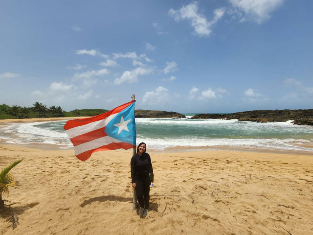 The author Vanessa Ramos, standing next to the Puerto Rico flag at Mar Chiquita