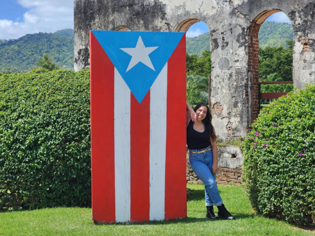 The author Vanessa Ramos, posing for a photo beside a Puerto Rico flag