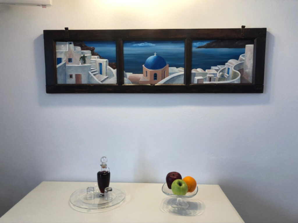 A bottle of Vinsanto on the table with an artwork of Santorini above