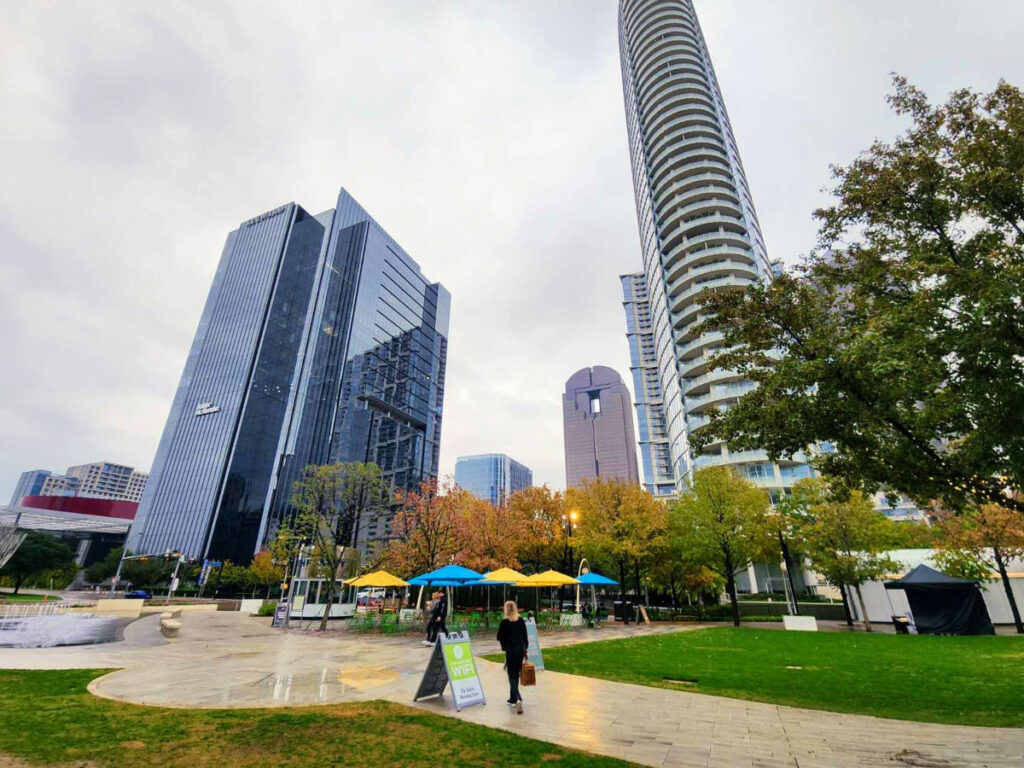 Author Sarah Heath walking in Klyde Warren Park with the city skyline in the background