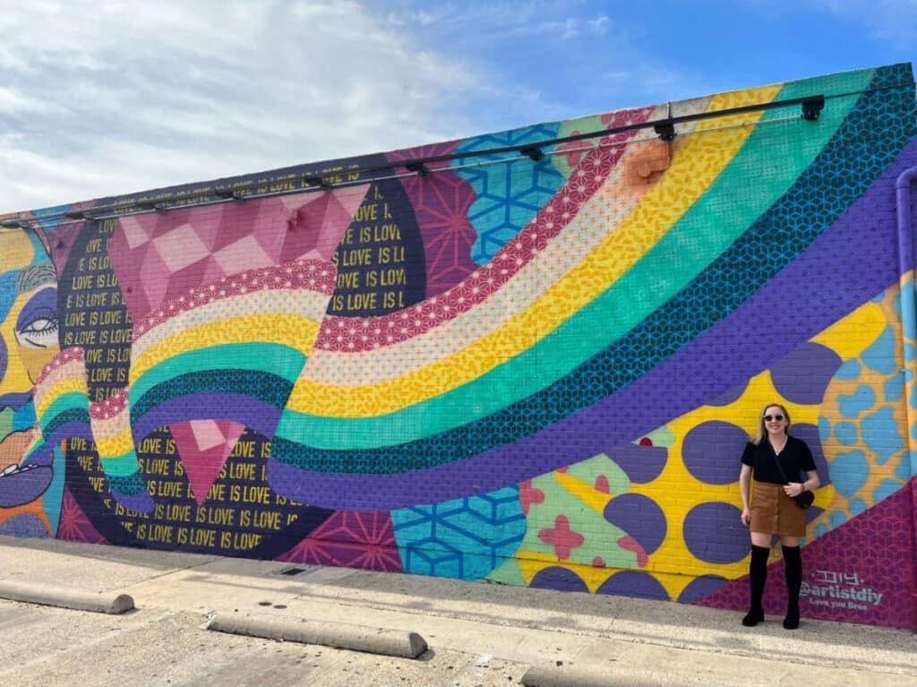 The author, Sarah Heath smiling for a photo with the colorful mural in Oak Lawn