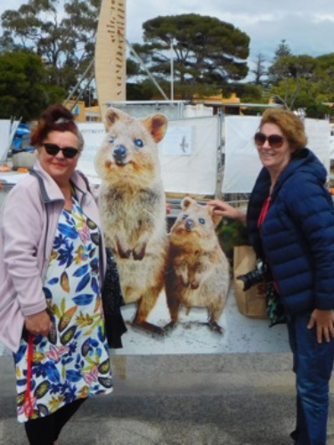 The author Lisa Ikin, smiling for a photo in front of the welcome signage of Rottnest Island/Wadjemup