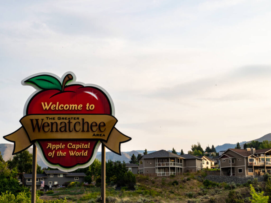 A welcome signage of Wenatchee shaped in an apple with the neighborhood in the background