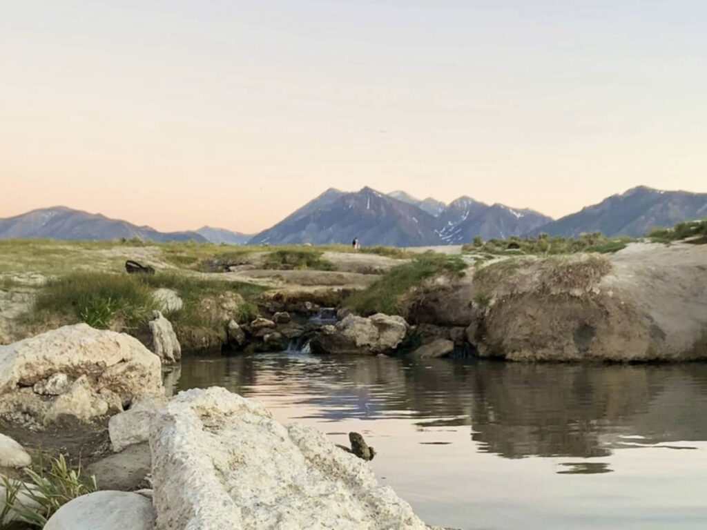 Picturesque view of the natural hot springs with mountain views at Wild Willy’s Hot Spring at dusk