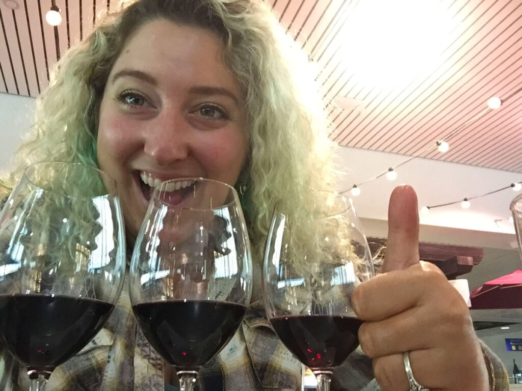Author Jess Levy giving a thumbs up, with three wine glasses