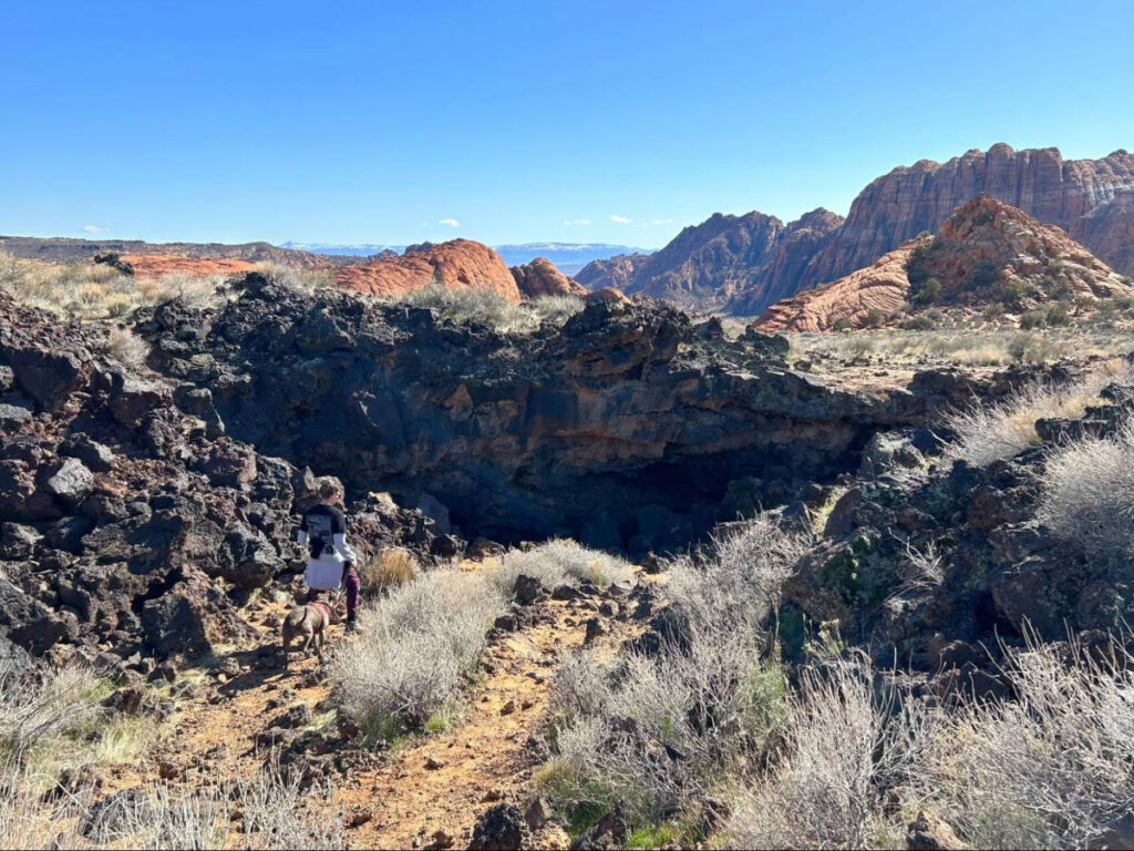 A hiker and a dog entering the lava tunnels at Snow Canyon State Park