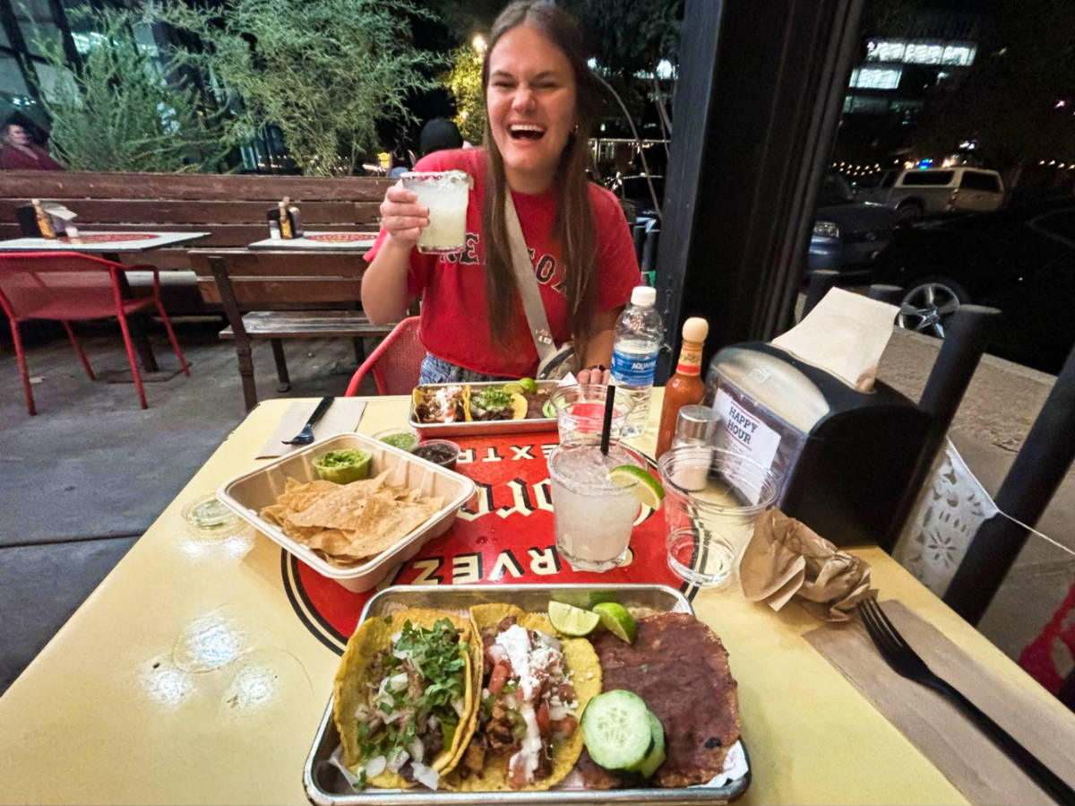 A woman holding a glass of margarita with tacos on the table