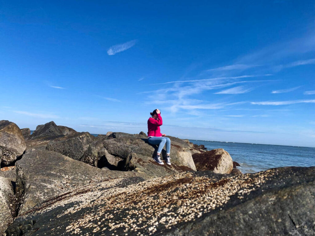 A woman enjoying the peaceful beach scenery at Vilano Beach while sitting on the rocks