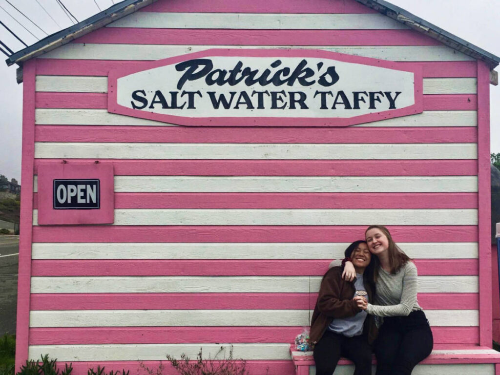 Two women posing for a photo at the pink exterior of Patrick’s Salt Water Taffy Shop