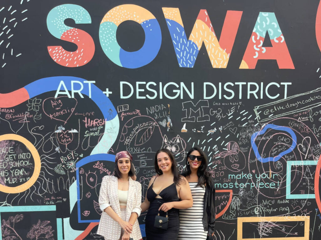 The author Claudicet Pena with her best friend, and sister, posing for a photo in front of the mural in SoWa Art + Design District